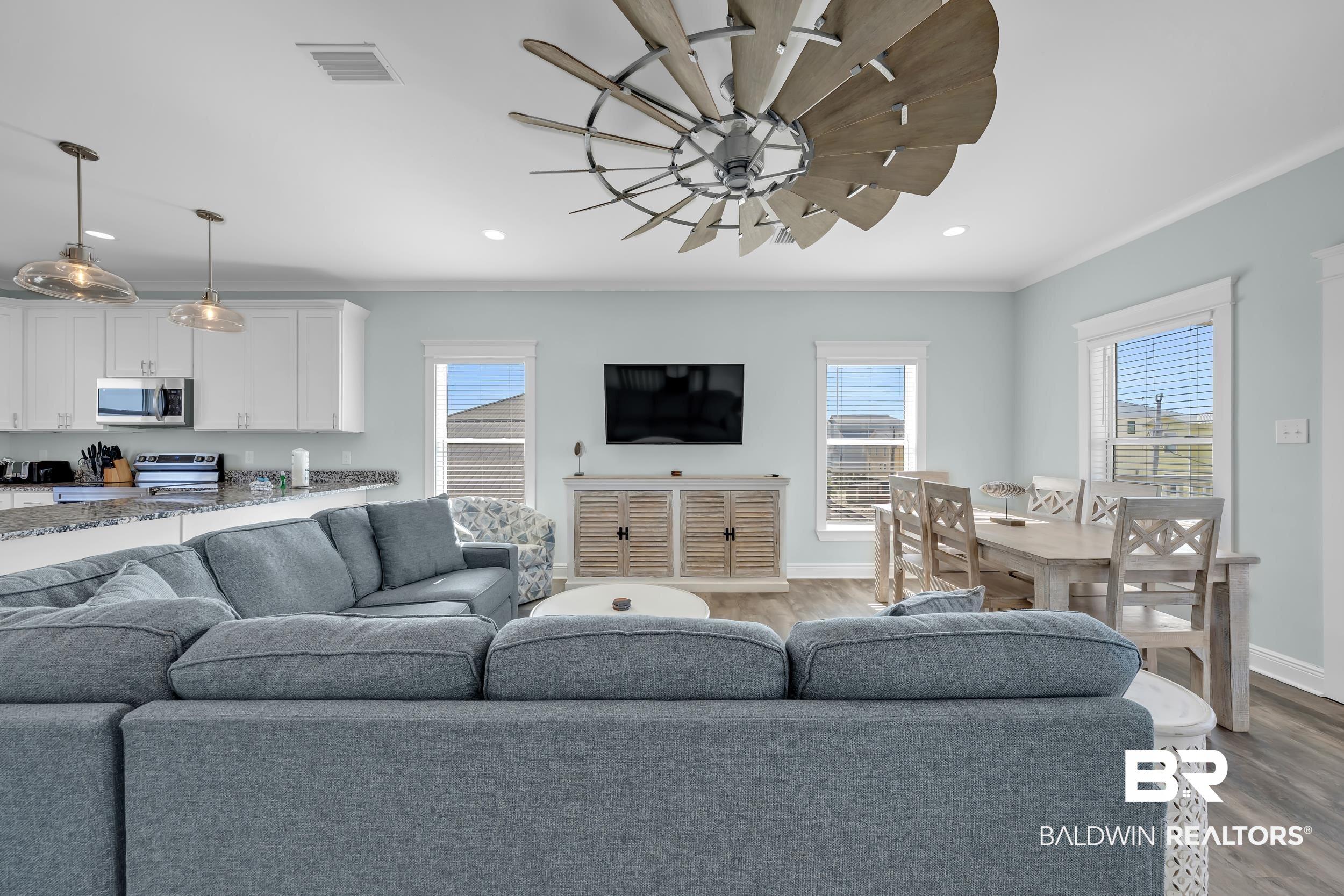 Image 3: Open-concept living space featuring wood-finish flooring, a contemporary ceiling fan, and multiple windows
