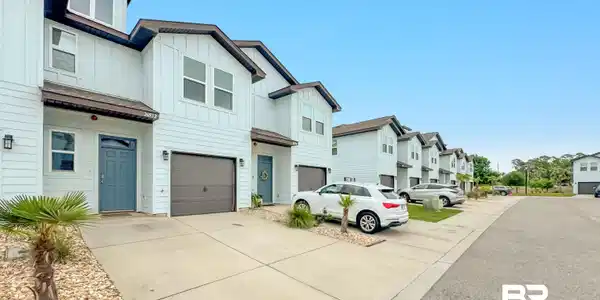 Image 3: Modern townhome-style residences featuring light-colored siding, a dark-toned roofline, and attached garages
