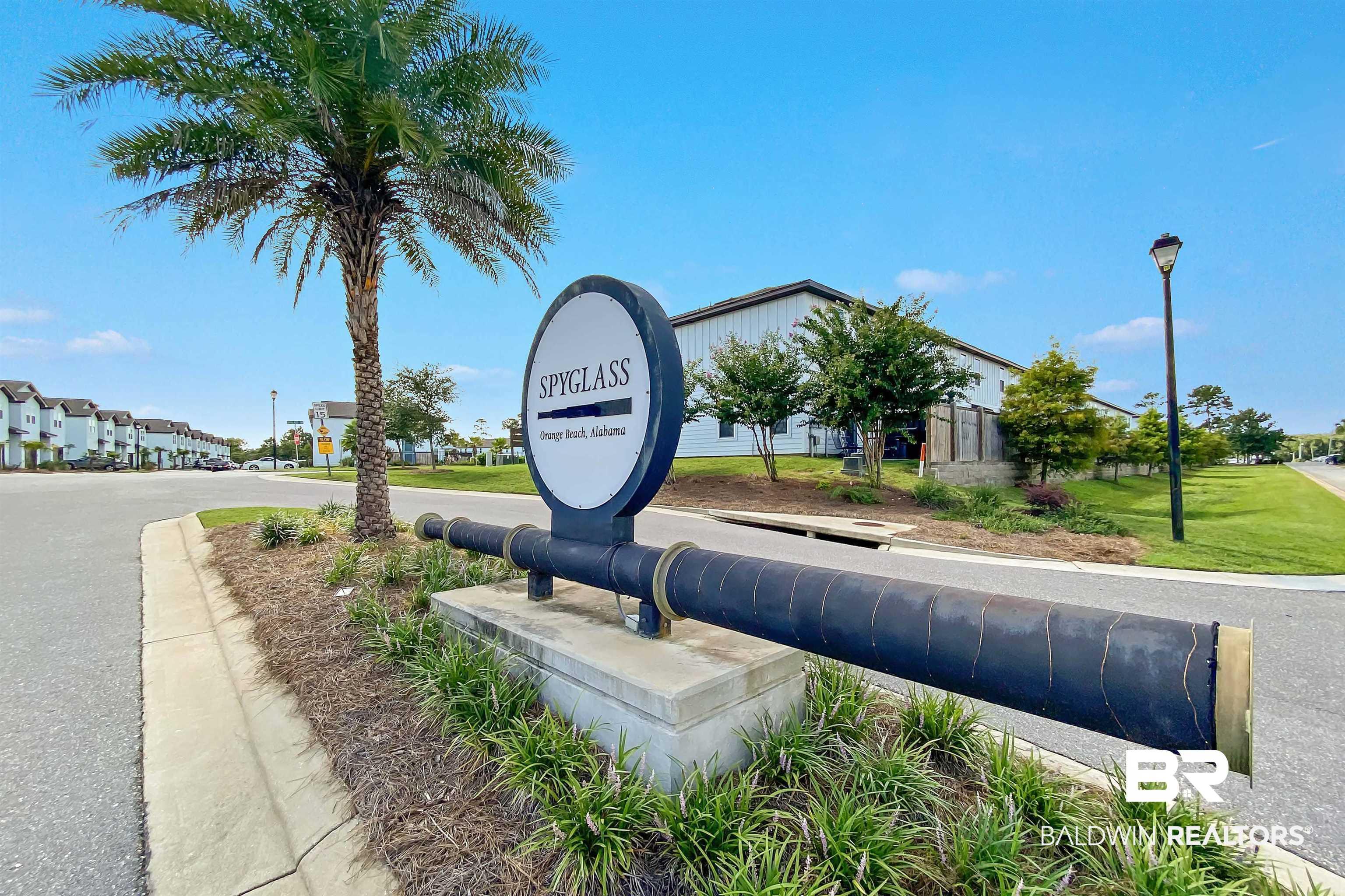 Image 4: Community entrance signage featuring a decorative cannon and a palm tree, with paved roadways, maintained landscaping, and multi-story structures in the background