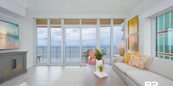 Image 2: Floor-to-ceiling glass doors open to a balcony with metal railings and water