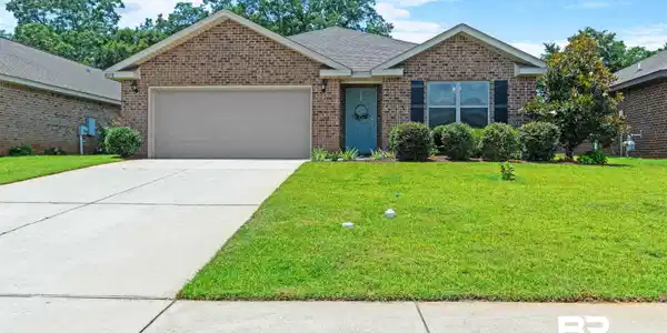 Image 2: Brick facade residence featuring an attached garage with a paved driveway, a manicured front lawn, and mature landscaping