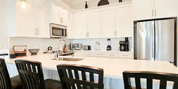 Image 2: Contemporary kitchen featuring white cabinetry, a large center island with seating, stainless steel appliances, a tile backsplash, and pendant lighting