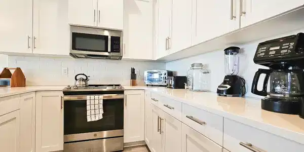 Image 3: Modern kitchen with white shaker cabinetry, stainless steel appliances, a white subway tile backsplash, and light-toned countertops