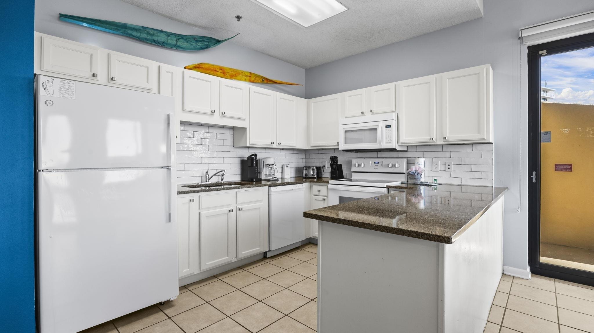 Image 4: Kitchen with white appliances, backsplash, white cabinetry, light tile patterned flooring, and dark stone countertops