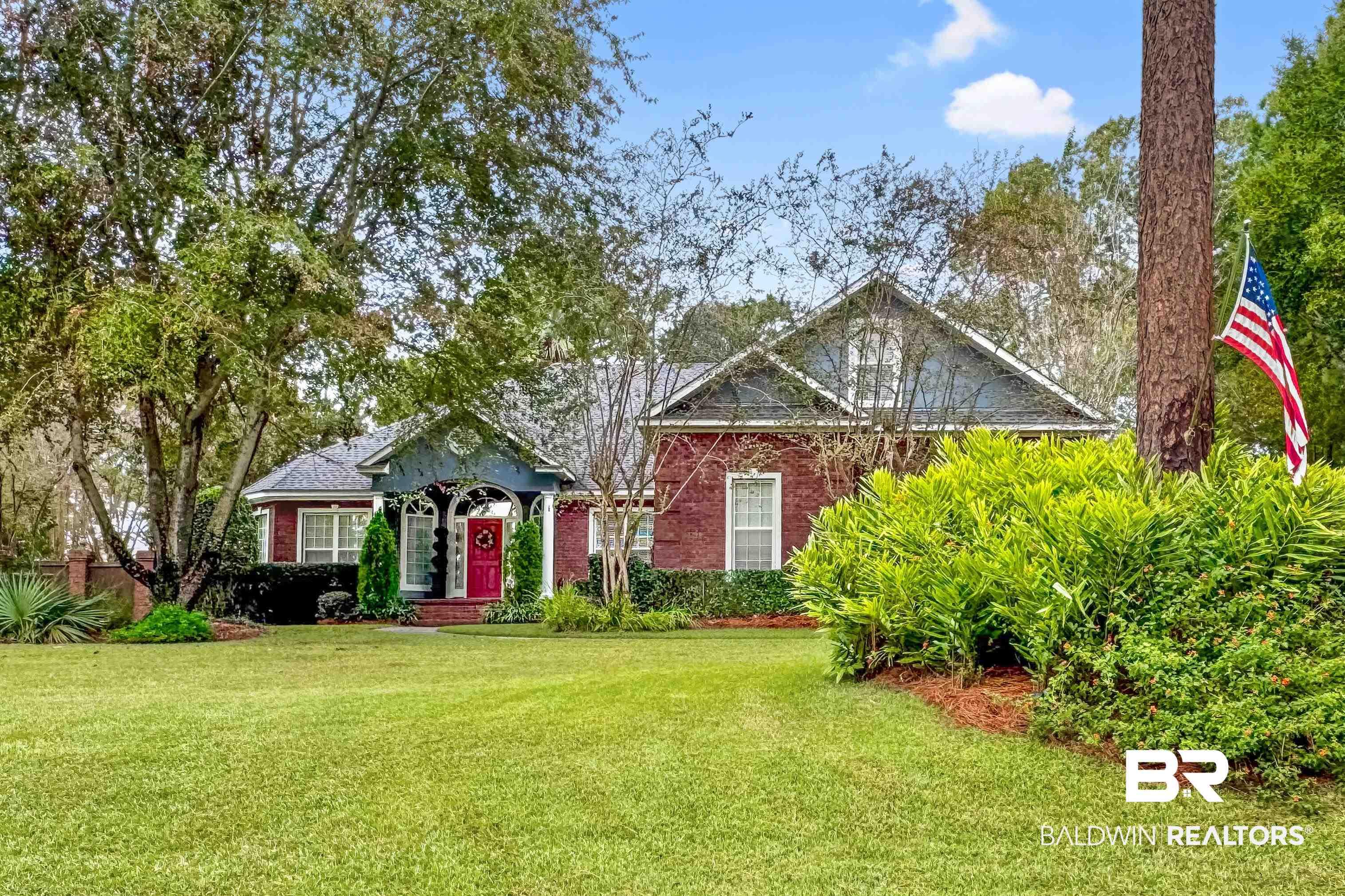 Image 1: Brick residence with a prominent red door and a decorative front porch