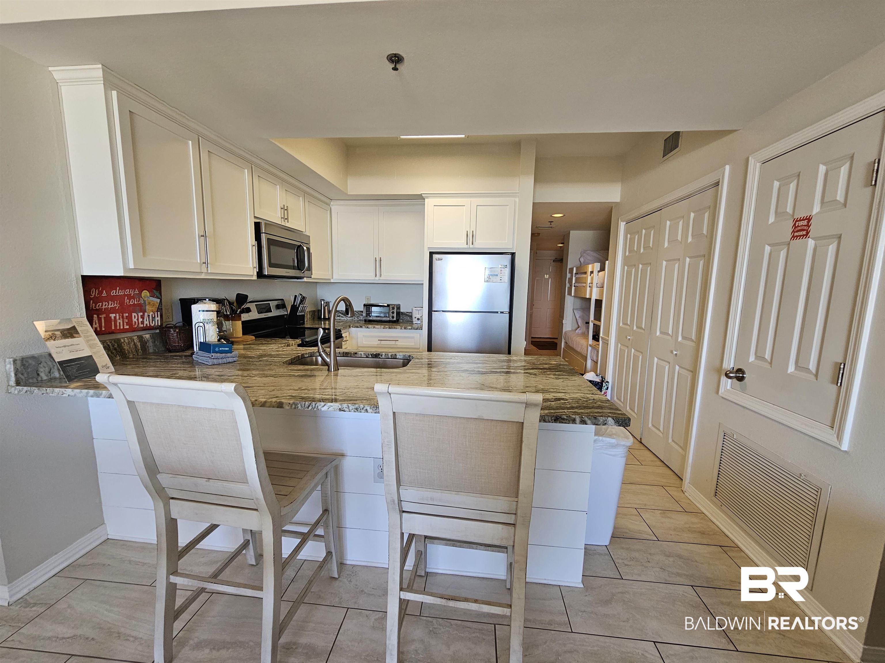 Image 3: Updated kitchen featuring white cabinetry, stainless steel appliances, "Fantasy Brown" counter tops with a large undermount  SS sink, and tile flooring!