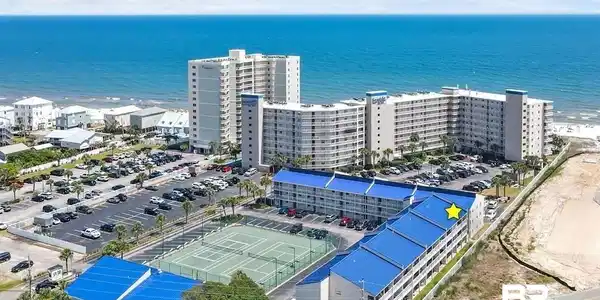 Image 3: Coastal multi-story building featuring a bright blue roofline, multiple balconies, and integrated parking