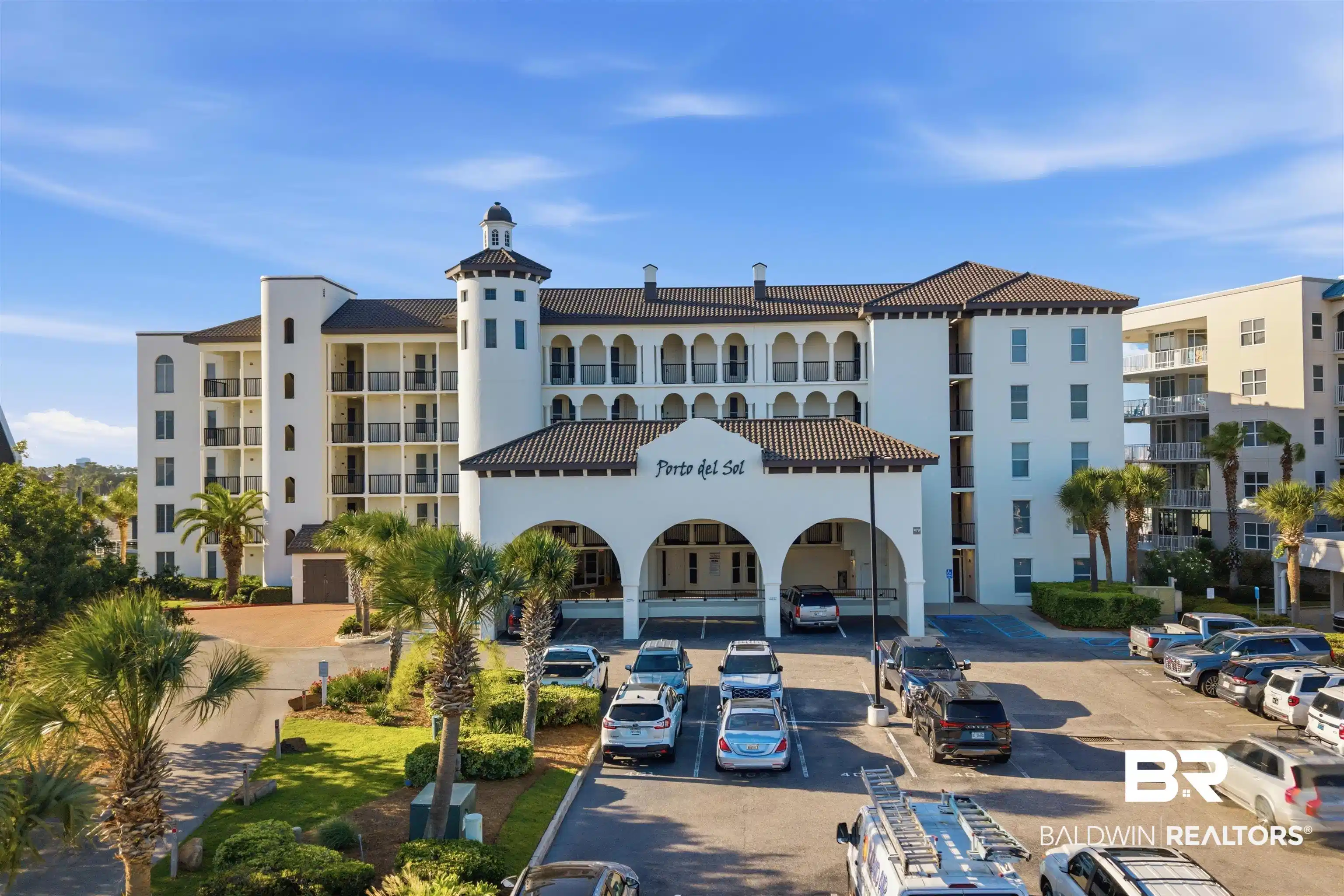 Image 1: Stately condominium building featuring a stucco exterior, tiled roof, and a prominent arched porte-coch&egrave;re entrance