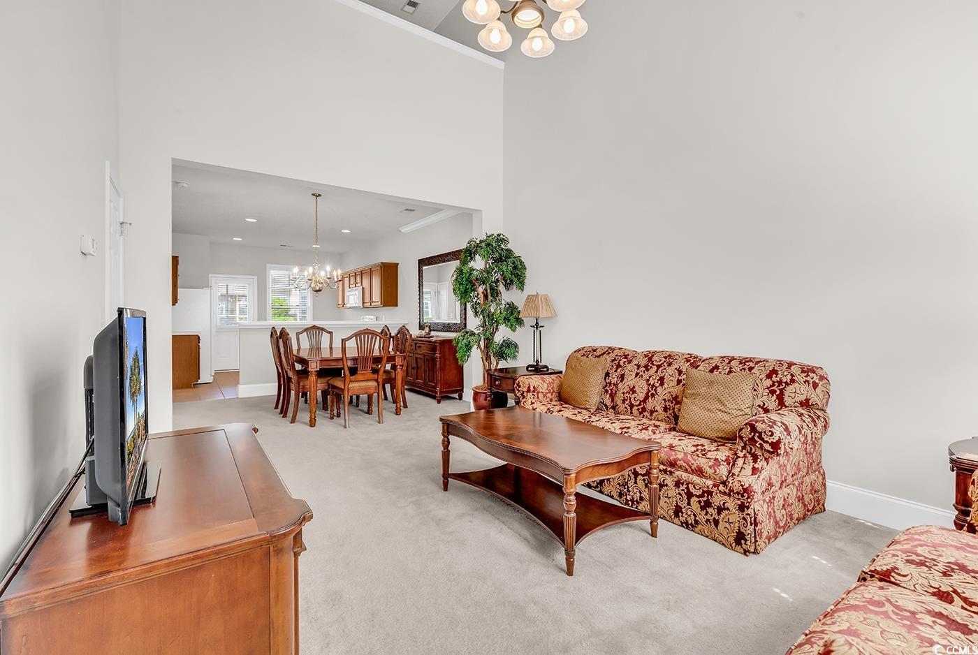 Image 4: Living area with a chandelier, light carpet, baseb