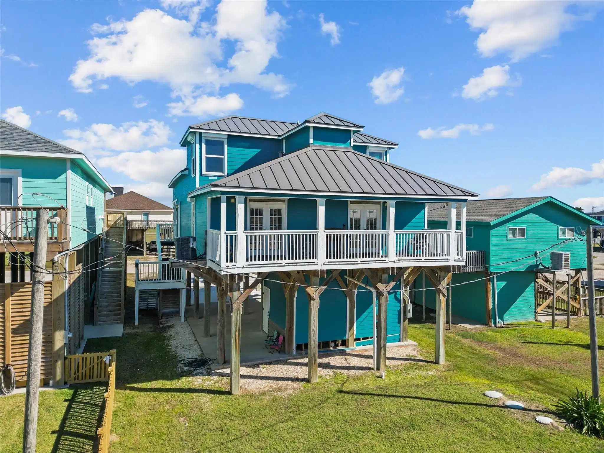 Image 1: Elevated coastal home with a bright blue exterior,