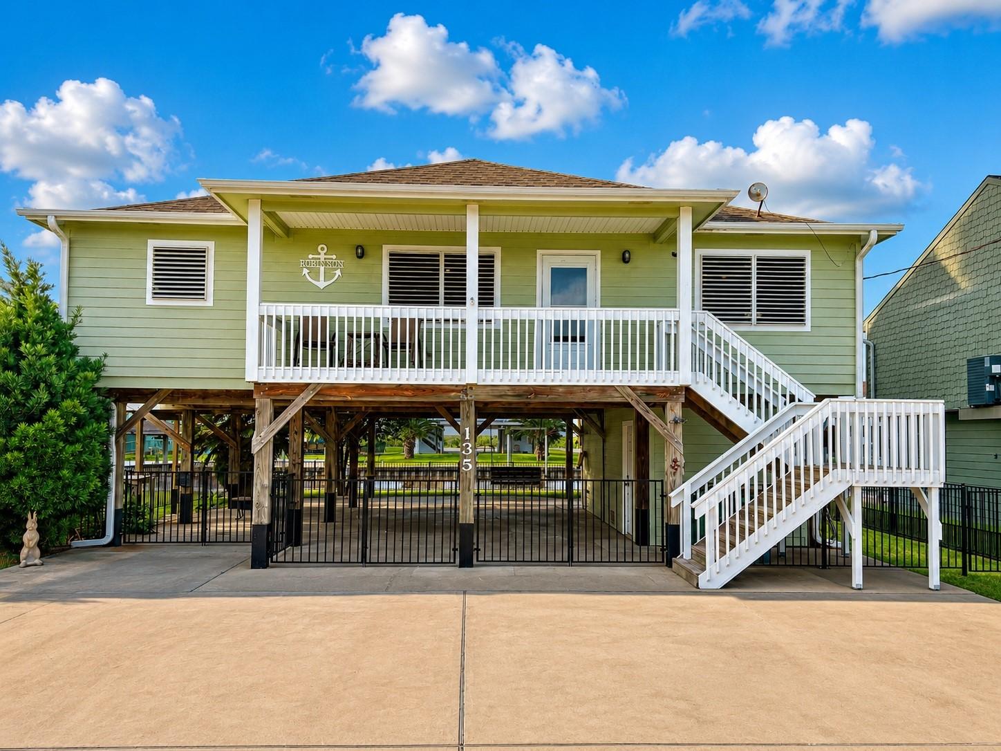 Image 1: This elevated home features a charming green exter