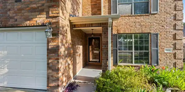 Image 2: A sheltered front porch framed by brick and landsc