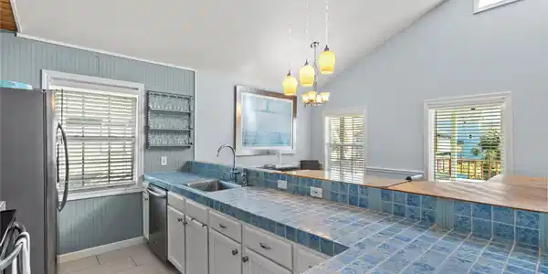 Image 3: The kitchen includes tile countertops, a double si
