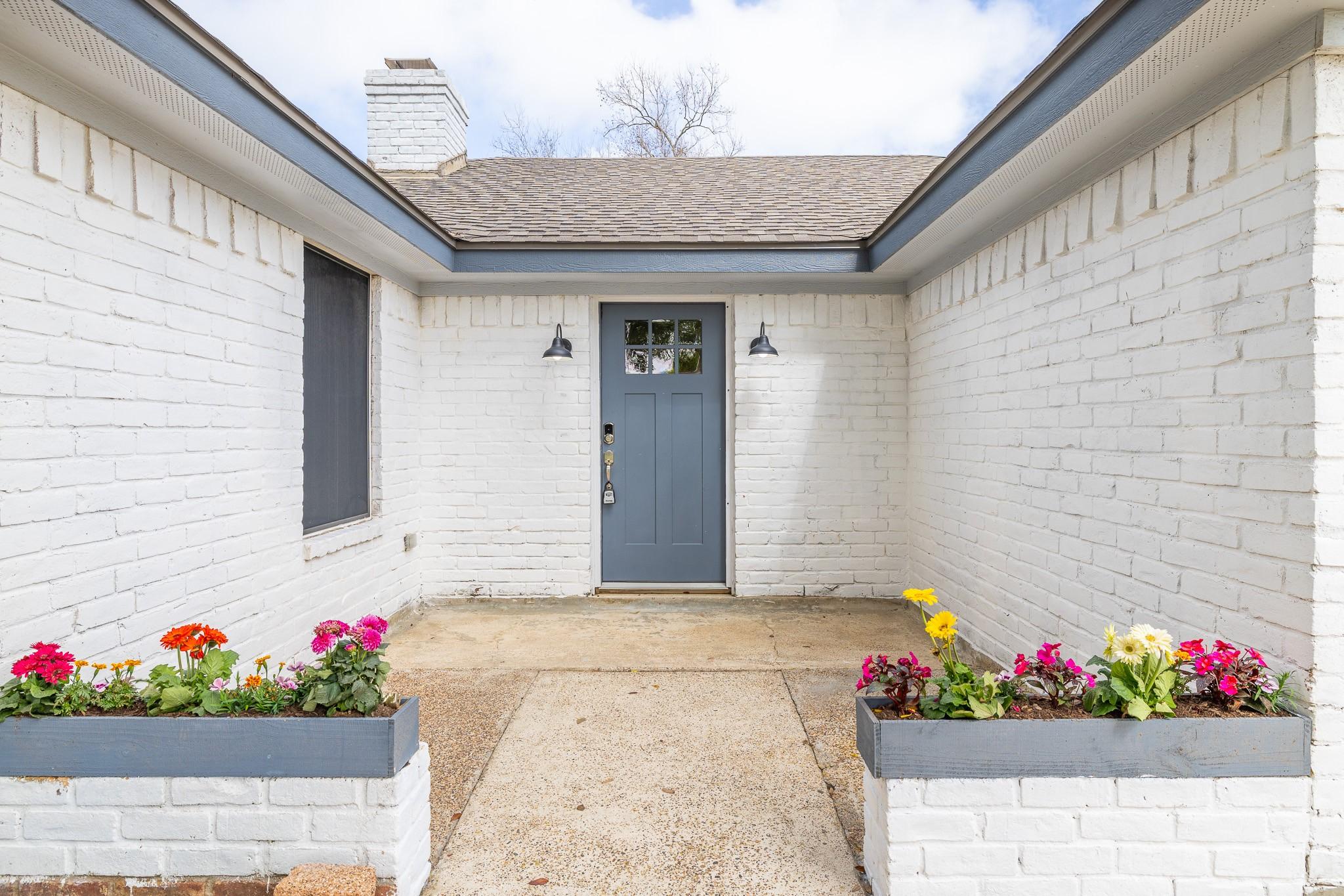 Image 2: The entrance is flanked by beautiful flowers and a