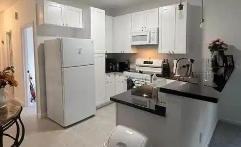 Image 3: This photo is a well-lit kitchen with white cabine
