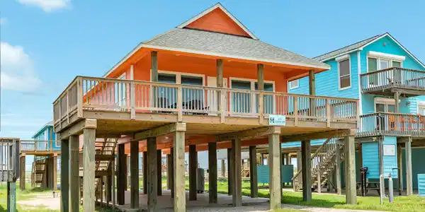 Image 2: This elevated beach house features a vibrant orang