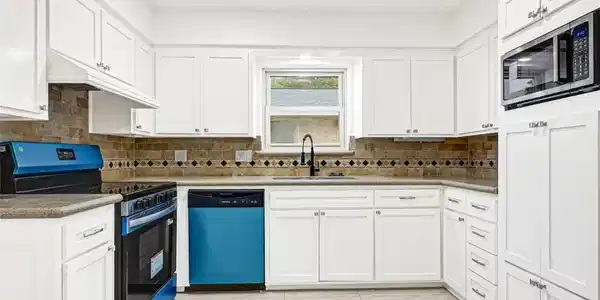 Image 2: This kitchen features modern white cabinetry, a sl