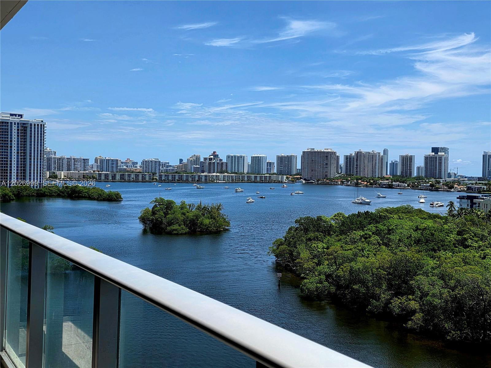 Image 2: The balcony captures wide water views with surrounding greenery, boats, and the city skyline beyond.