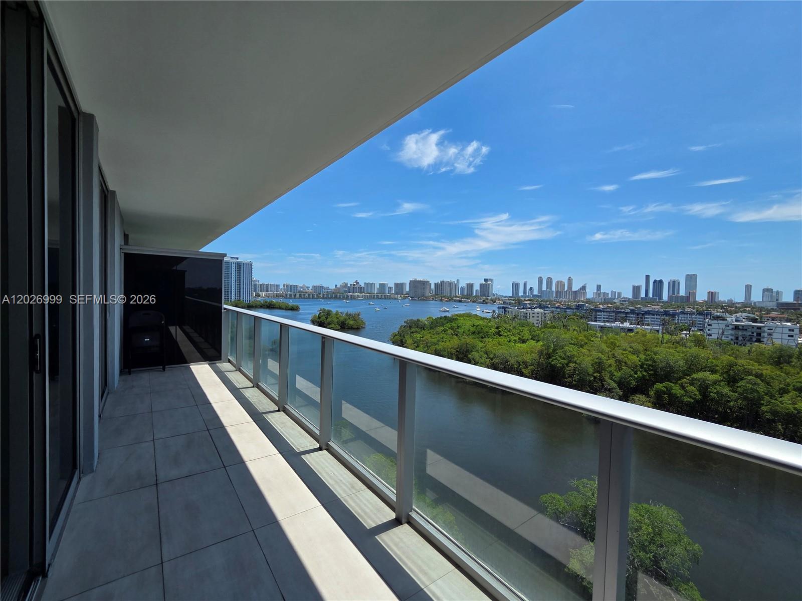 Image 4: Spacious balcony with glass railings and sweeping views over the waterway, treetops, and skyline. Th