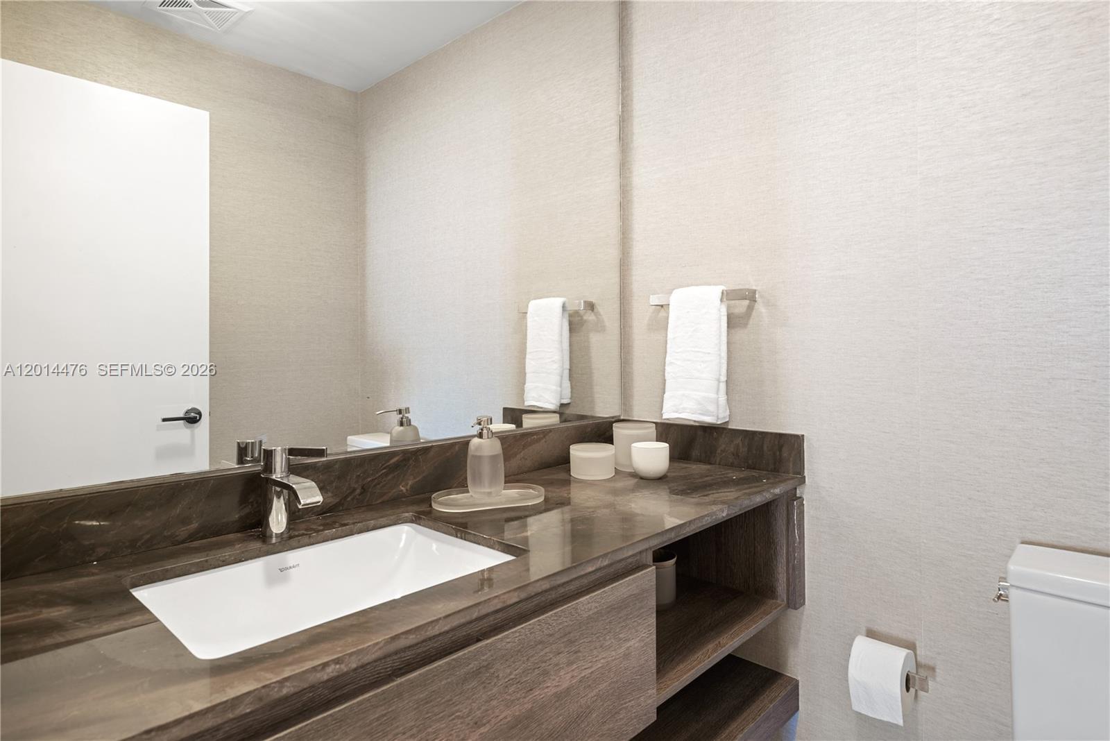 Image 4: Powder Room &ndash; The powder room offers a streamlined vanity with a dark stone countertop, underm