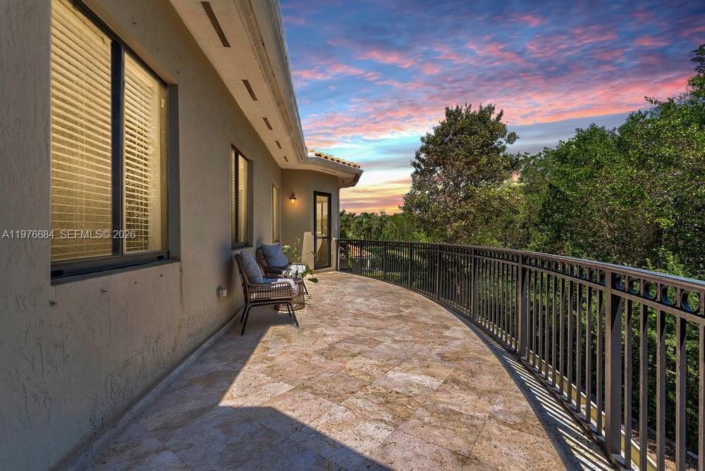Image 3: Curved upper-level balcony with travertine tile flooring, wrought-iron railing, and a small seating 