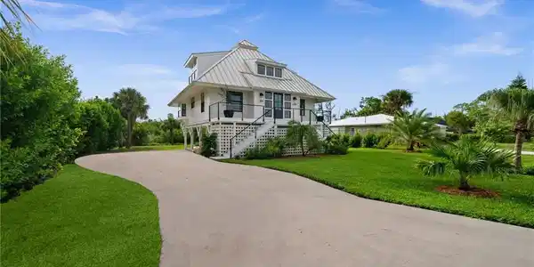 Image 2: Elevated coastal-style residence with a metal roof, white siding, and a spacious front lawn