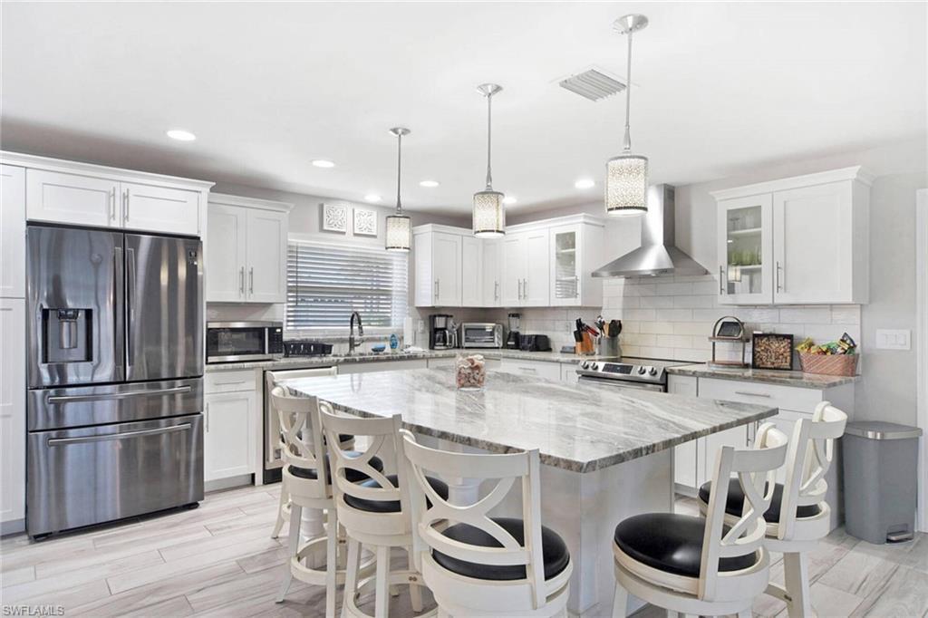 Image 2: Kitchen with appliances with stainless steel finishes, light stone countertops, white cabinetry, wall chimney range hood, and recessed lighting