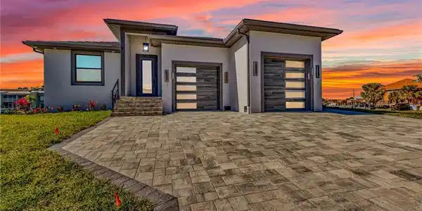 Image 2: View of front facade with stucco siding, decorative driveway, an attached garage, and a lawn