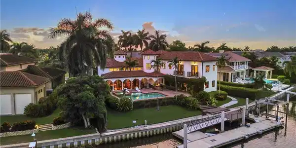 Image 3: Mediterranean-style residence featuring a terracotta tile roof, white stucco exterior, arched covered patio, private swimming pool, and a multi-slip dock with a boat lift