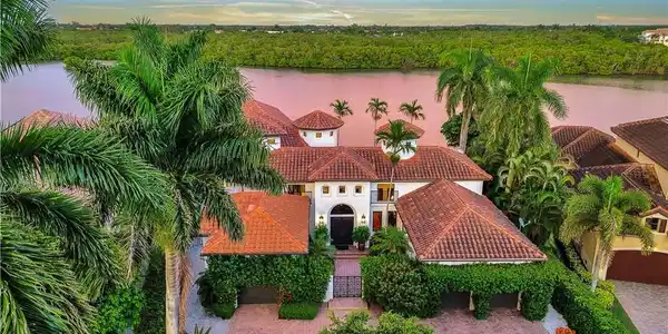 Image 4: Mediterranean-style residence featuring a terracotta tile roof, white stucco exterior, and lush tropical landscaping