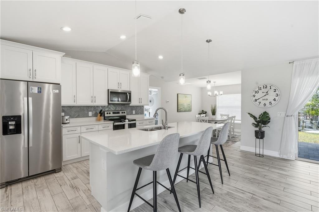 Image 4: Modern kitchen featuring a large center island with pendant lighting, stainless steel appliances, and white cabinetry