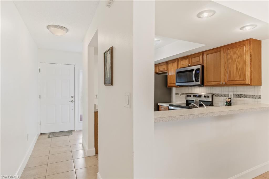 Image 2: Kitchen featuring backsplash, light tile patterned flooring, light countertops, stainless steel appliances, and brown cabinetry