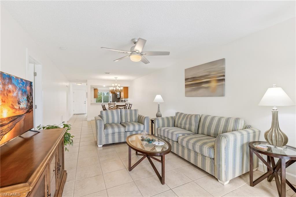 Image 3: Living area with light tile patterned flooring, a chandelier, a ceiling fan, and a textured ceiling