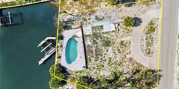 Image 4: Aerial view of property and surrounding area with property boundaries highlighted, a pool, and a large body of water  - Virtually Edited Image