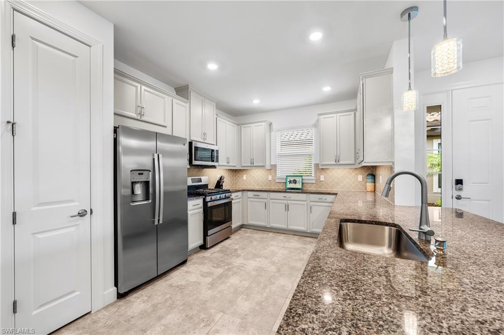 Image 2: Kitchen featuring white cabinetry, stainless steel appliances, speckled countertops, and a patterned tile backsplash