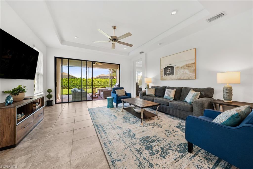 Image 3: Open-concept living area featuring tile flooring, a tray ceiling with a ceiling fan, and recessed lighting