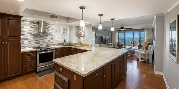 Image 3: Gourmet kitchen featuring a large island with a stone-finish countertop, rich wood cabinetry, stainless steel appliances, and a mosaic tile backsplash