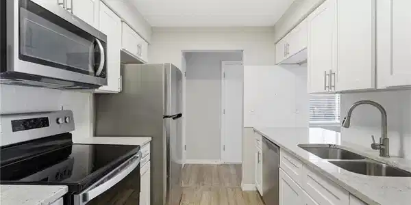 Image 2: Kitchen featuring stainless steel appliances, tasteful backsplash, light stone countertops, white cabinets, and light wood-style flooring