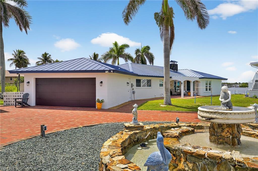 Image 4: Ranch-style house featuring a standing seam roof, an attached garage, a metal roof, decorative driveway, and a chimney