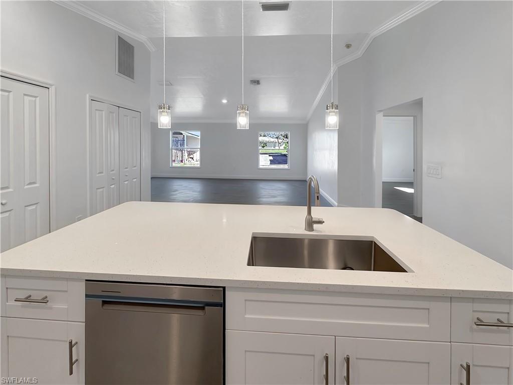Image 3: Kitchen featuring white cabinetry, stainless steel dishwasher, light stone countertops, ornamental molding, and hanging light fixtures