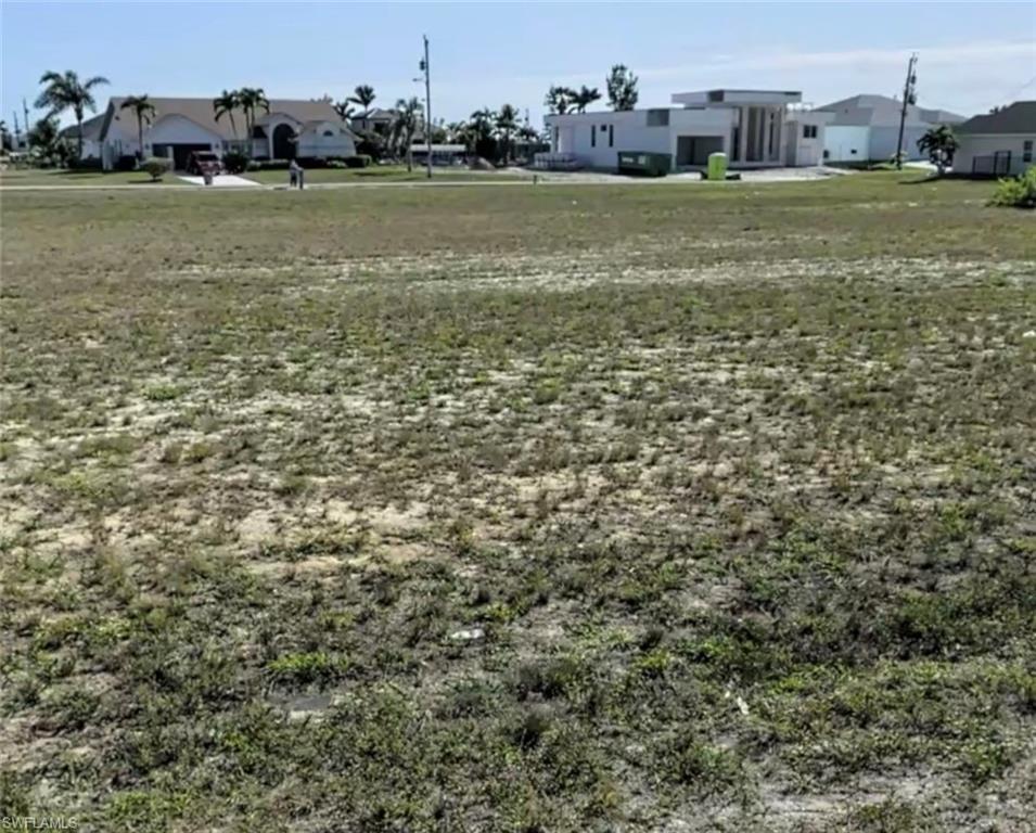Image 3: Expansive vacant lot featuring sparse natural ground cover and distant residential structures