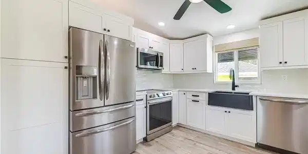 Image 2: Modern kitchen featuring white shaker cabinetry, stainless steel appliances, wood-finish flooring, recessed lighting, and a black farmhouse sink with a matching faucet