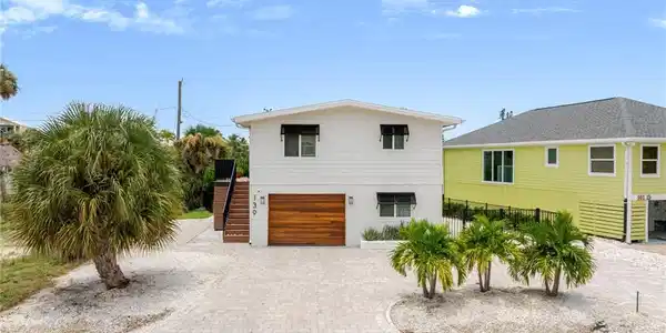 Image 4: White exterior with horizontal siding, wood-finish garage door, and black window awnings