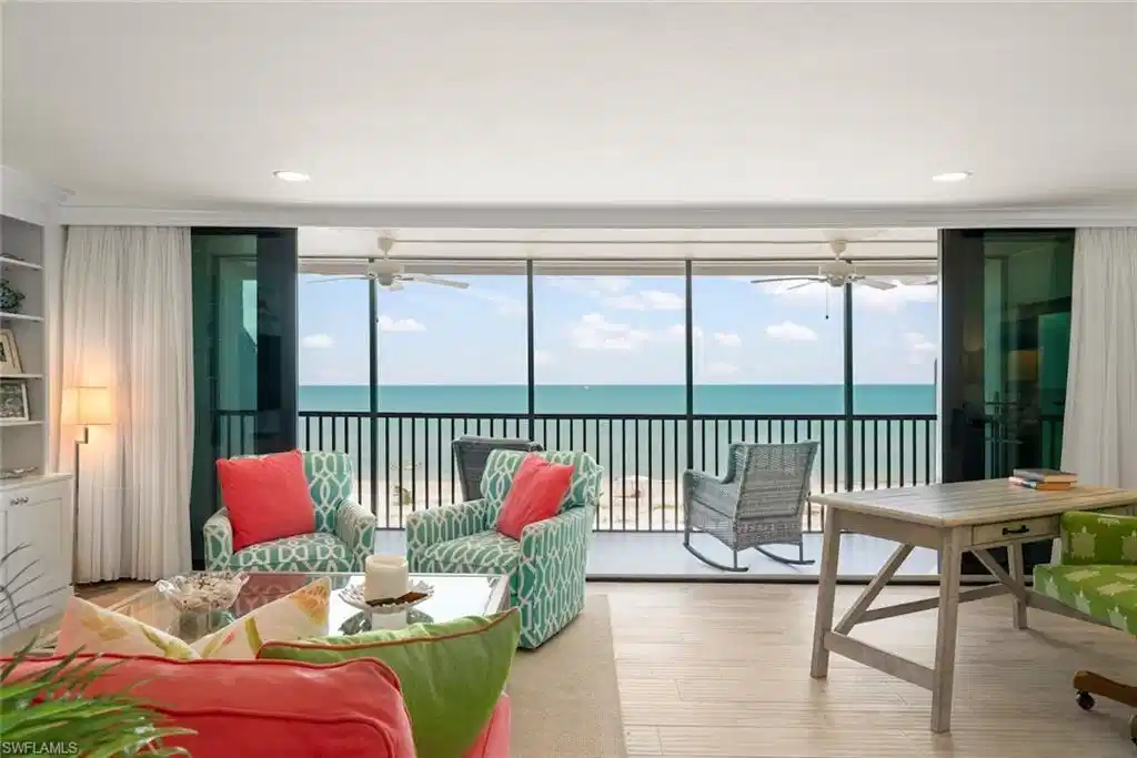 Image 1: Living area featuring floor-to-ceiling sliding glass doors, light wood-finish flooring, a built-in wall unit with display shelving, recessed lighting, and direct access to an outdoor balcony with water views