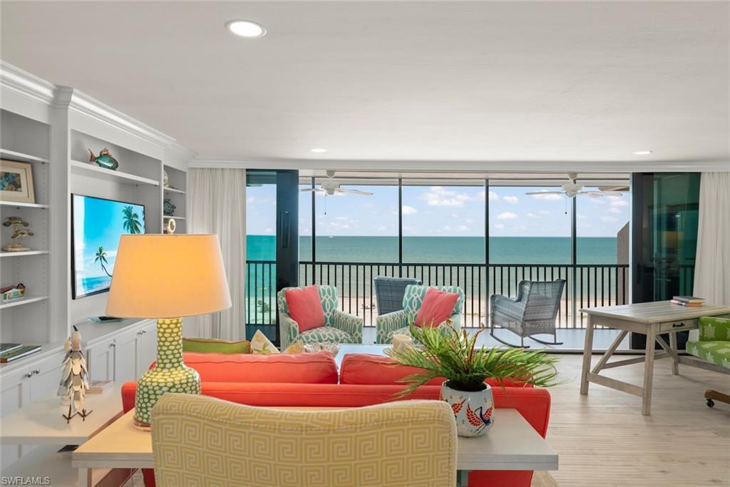 Image 2: Living area featuring floor-to-ceiling sliding glass doors, light wood-finish flooring, a built-in wall unit with display shelving, recessed lighting, and direct access to an outdoor balcony with water views