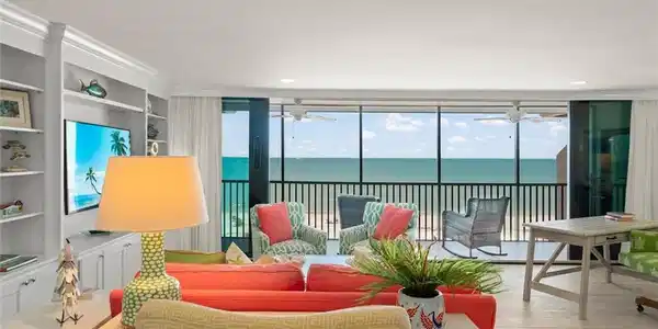 Image 2: Living area featuring floor-to-ceiling sliding glass doors, light wood-finish flooring, a built-in wall unit with display shelving, recessed lighting, and direct access to an outdoor balcony with water views