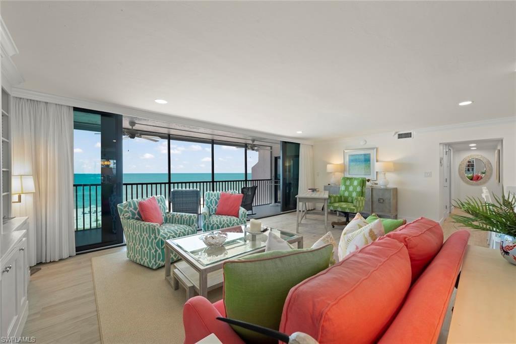 Image 3: Living area featuring floor-to-ceiling sliding glass doors, light wood-finish flooring, a built-in wall unit with display shelving, recessed lighting, and direct access to an outdoor balcony with water views