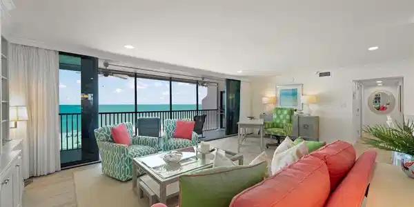 Image 3: Living area featuring floor-to-ceiling sliding glass doors, light wood-finish flooring, a built-in wall unit with display shelving, recessed lighting, and direct access to an outdoor balcony with water views