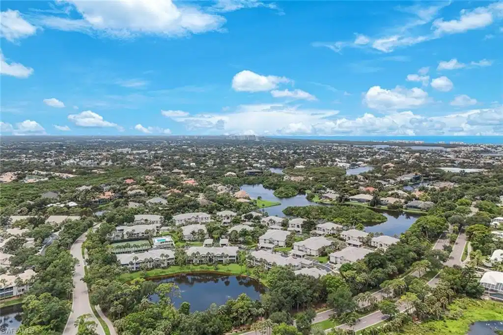 Image 1: Expansive aerial perspective showcasing a residential community with abundant green spaces, multiple water features, and distant coastal elements