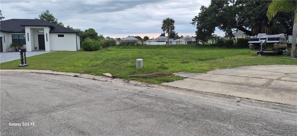 Image 3: Expansive cleared lot with established grass, featuring existing curb cut for driveway access